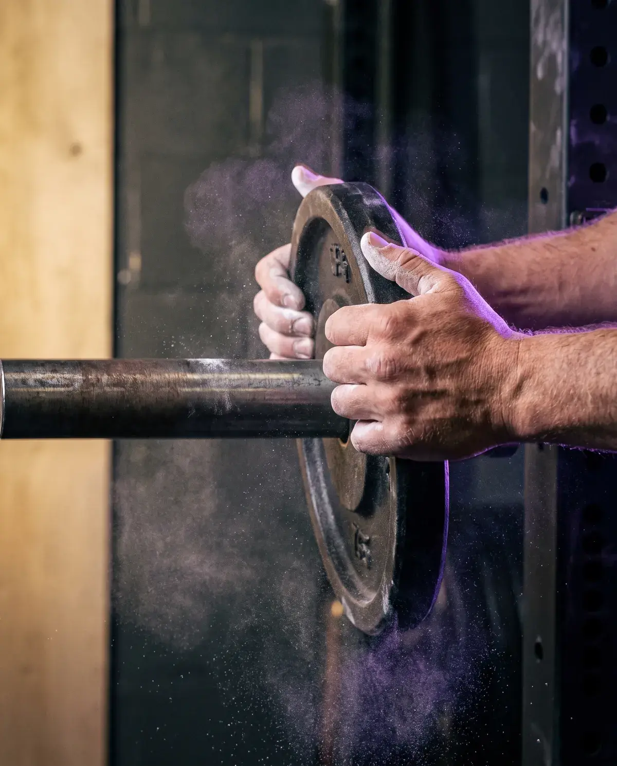 Chalked hands sliding an iron plate onto a barbell